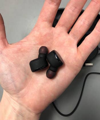 reviewer holding the black earbuds in their hand