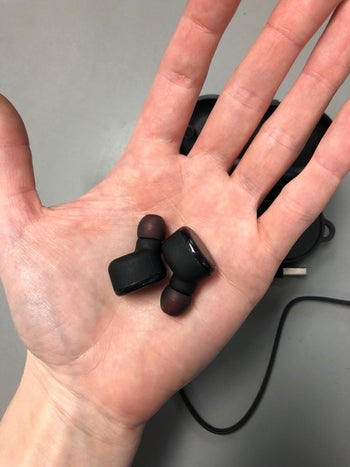 reviewer holding the black earbuds in their hand