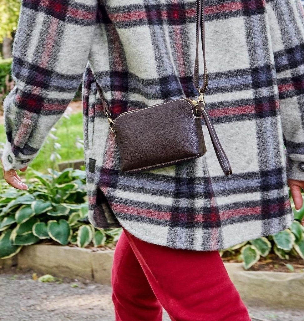A person wearing the bag over a plaid jacket