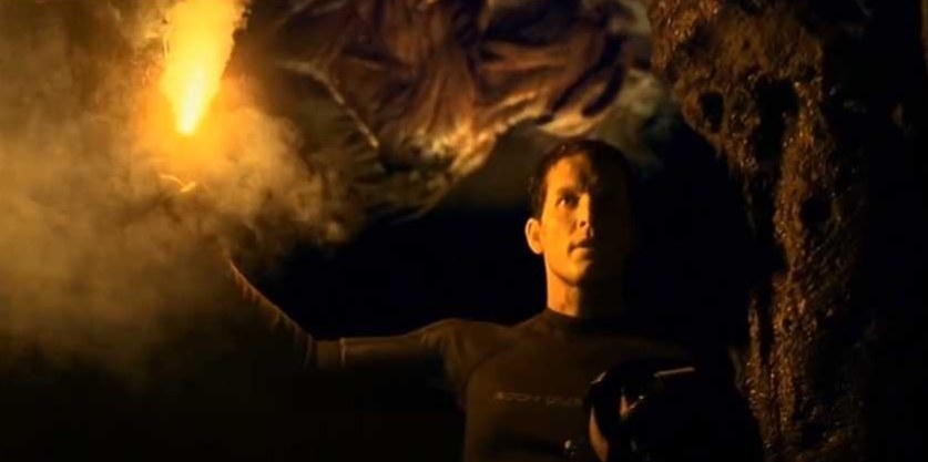 Man holds a flare in a cave and a monster is behind him on the ceiling