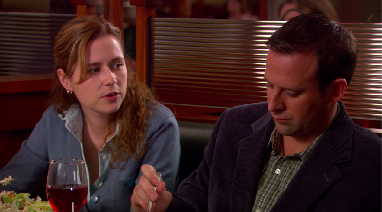 Pam wearing a sweater and button down top next to a man at a restaurant