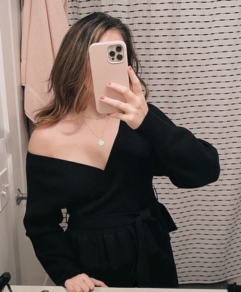 A customer review photo of them wearing the sweater, off the shoulder, in black