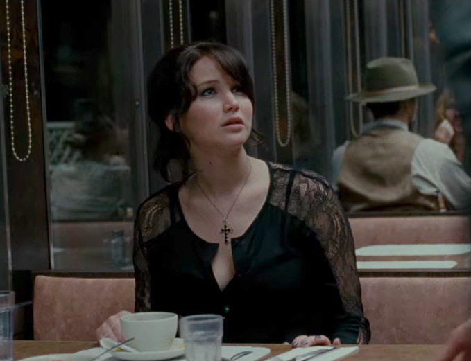 Jennifer Lawrence at a diner table with a black cross necklace