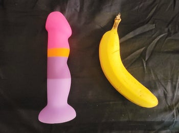 Pink stripe dildo next to banana to demonstrate size