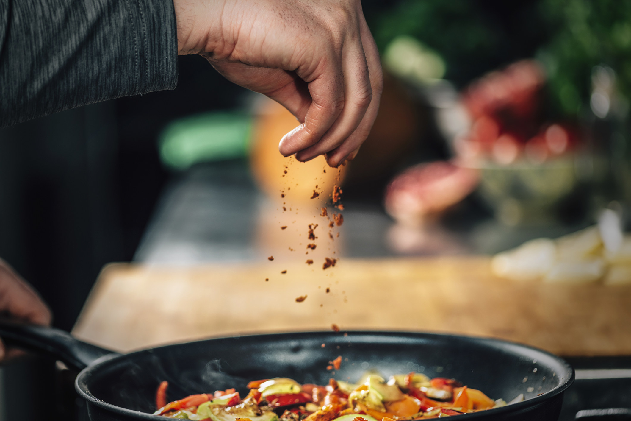 A chef seasons their food while cooking