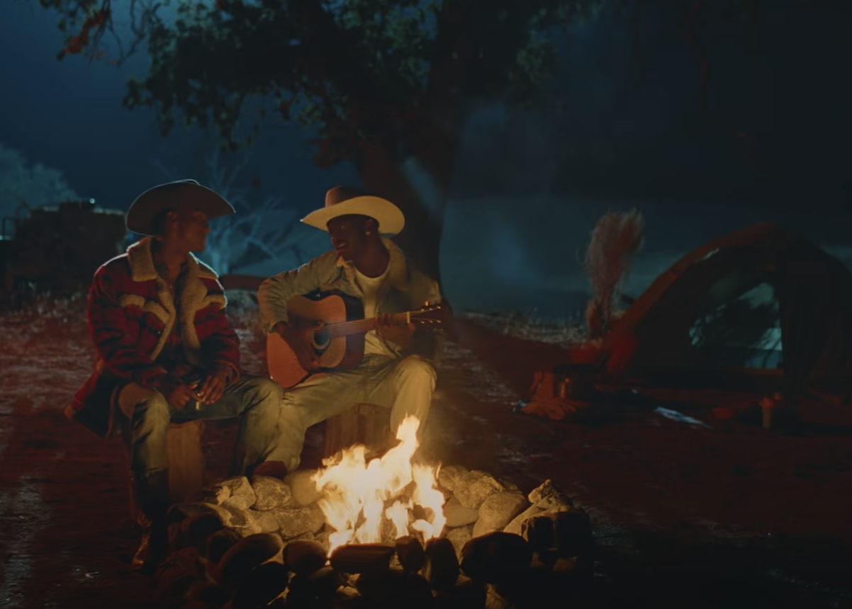 A scene from the That&#x27;s What I Want video with Lil Nas X playing the guitar as he and Yai sit at a campfire