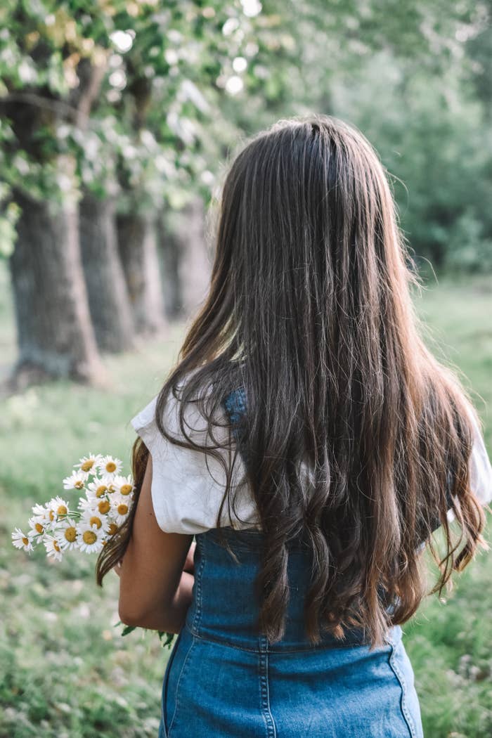Back view of a girl with very long hair holding a bunch of daisies