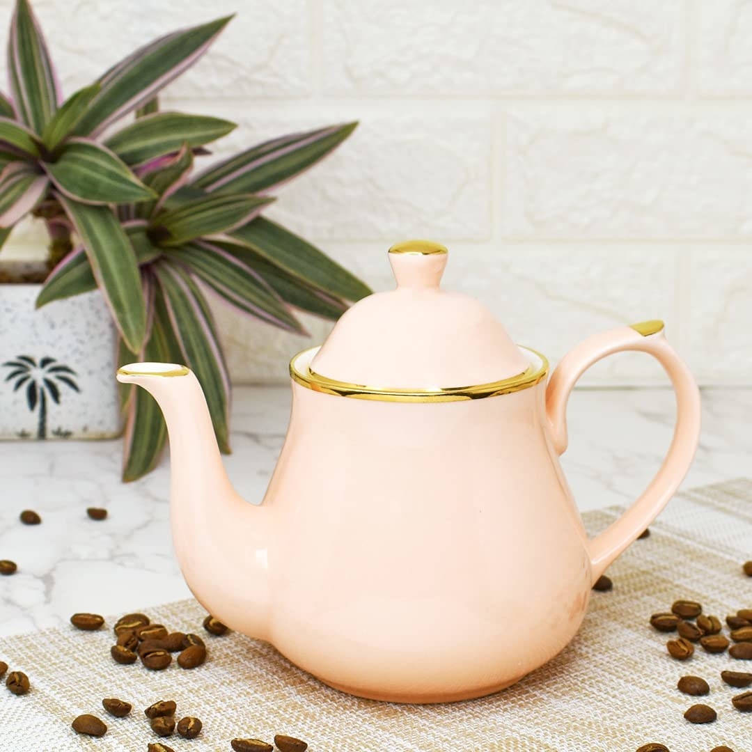 A pink kettle with a golden rim with coffee beans beside it