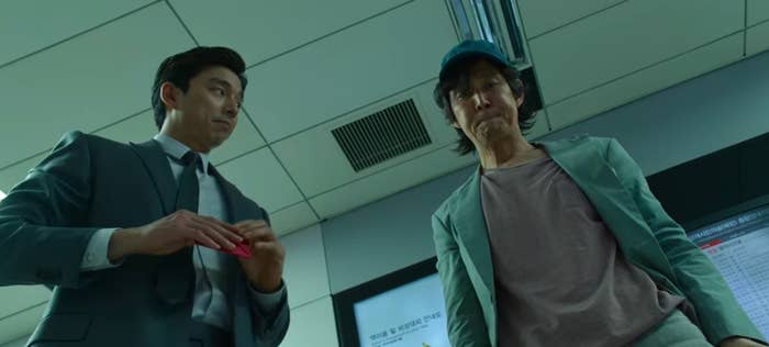 The recruiter stands with Gi-hun in a train station