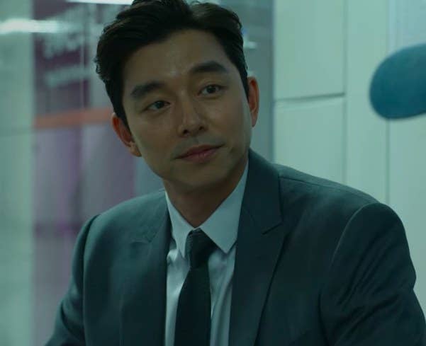 The recruiter — a man in a suit — sits in a train station looking at Gi-hun