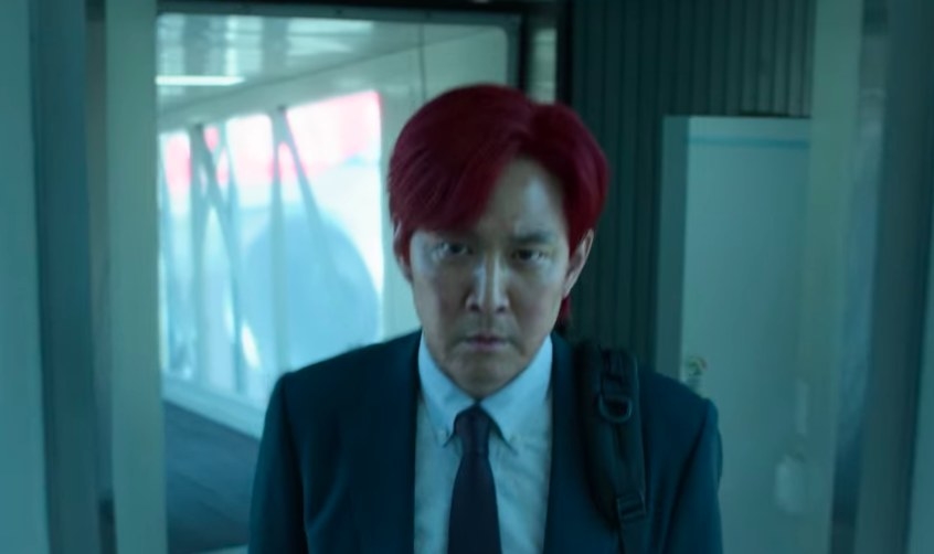 A red-haired Gi-hun walks out of an airport tunnel with a determined look on his face
