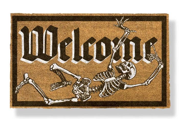 The rectangular mat says &quot;Welcome&quot; in old black font with white borders and a black and white skeleton below