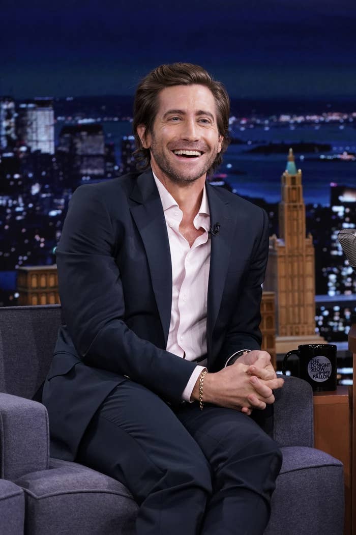 Gyllenhaal smiles while sitting on a chair