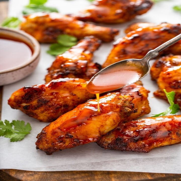 Spooning hot honey sauce onto crispy chicken wings.