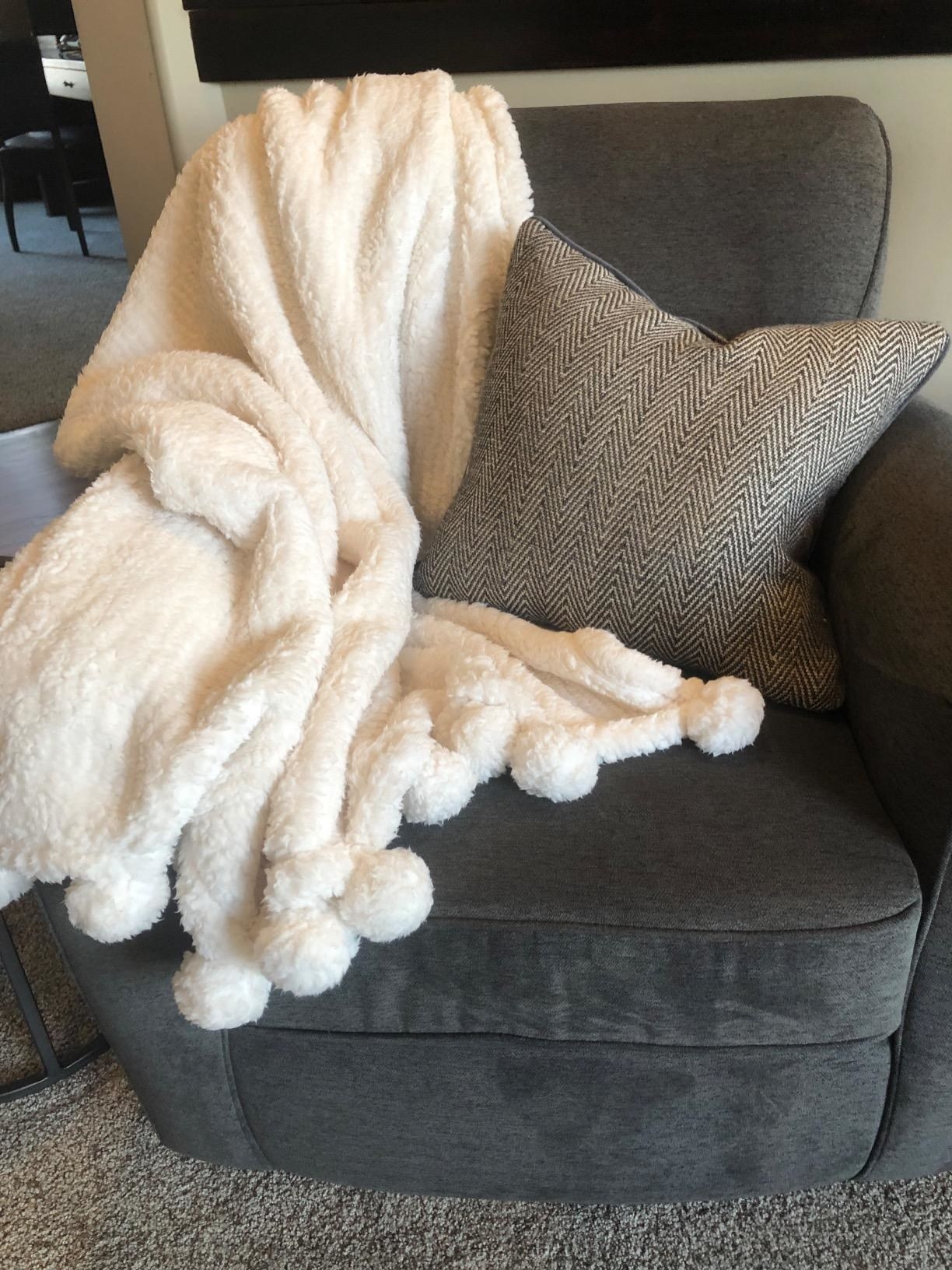 Reviewer photo of the white fluffy fleece blanket draped on a dark grey chair