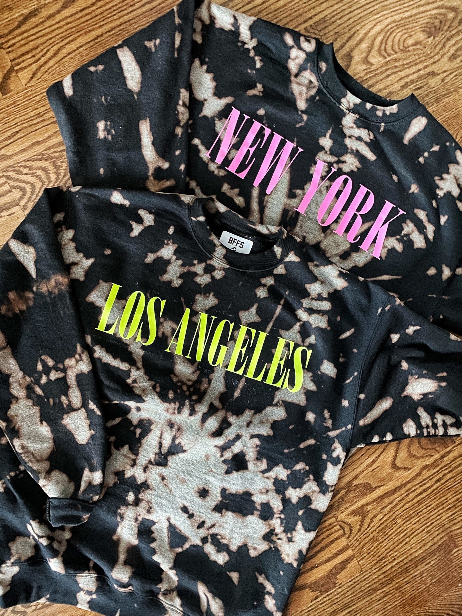 two black sweatshirts with acid wash tie dye, one says &quot;los angeles&quot; on yellow the other says &quot;new york&quot; in pink