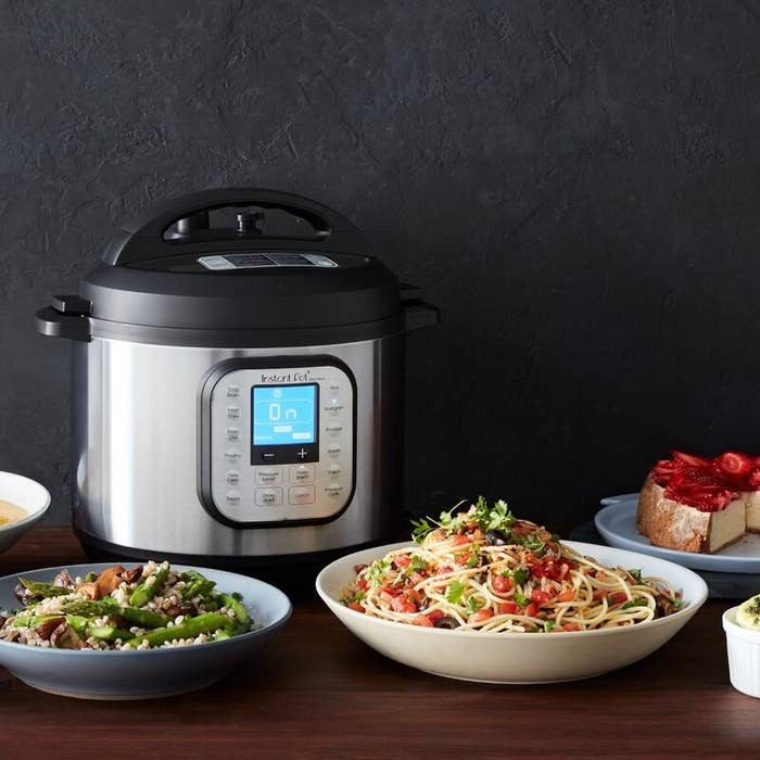 The instant pot in front of a pasta entree and side dish