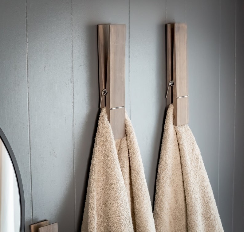 two jumbo clothespin towel holders mounted to a wall, each holding a beige towel