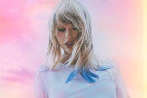 Taylor Swift looks down with rocking a glittery heart around one eye as she stands against a colorful sky