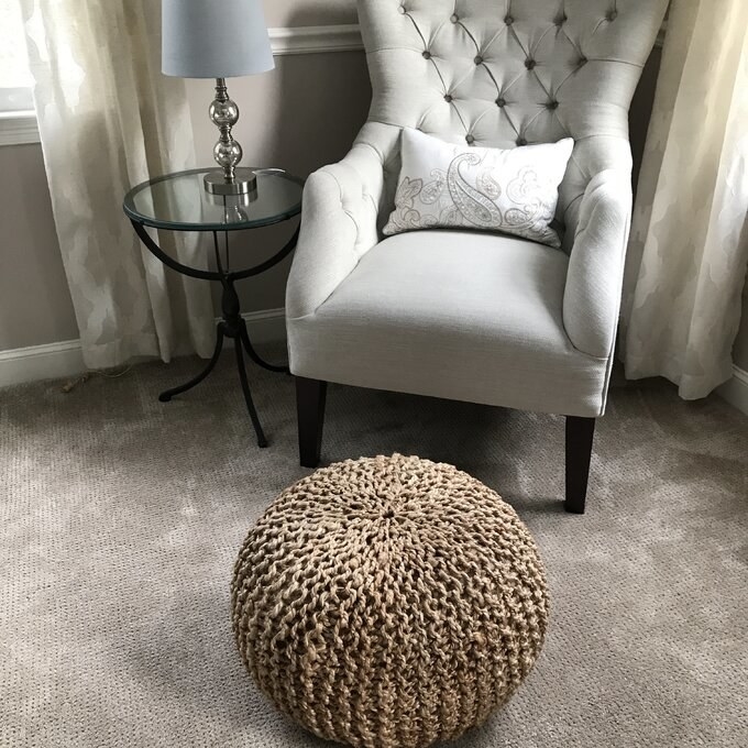 A reviewer&#x27;s photo of the beige pouf in front of a chair