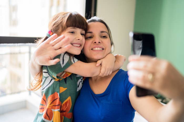 Smiling young girl embracing a smiling woman, who&#x27;s taking a selfie