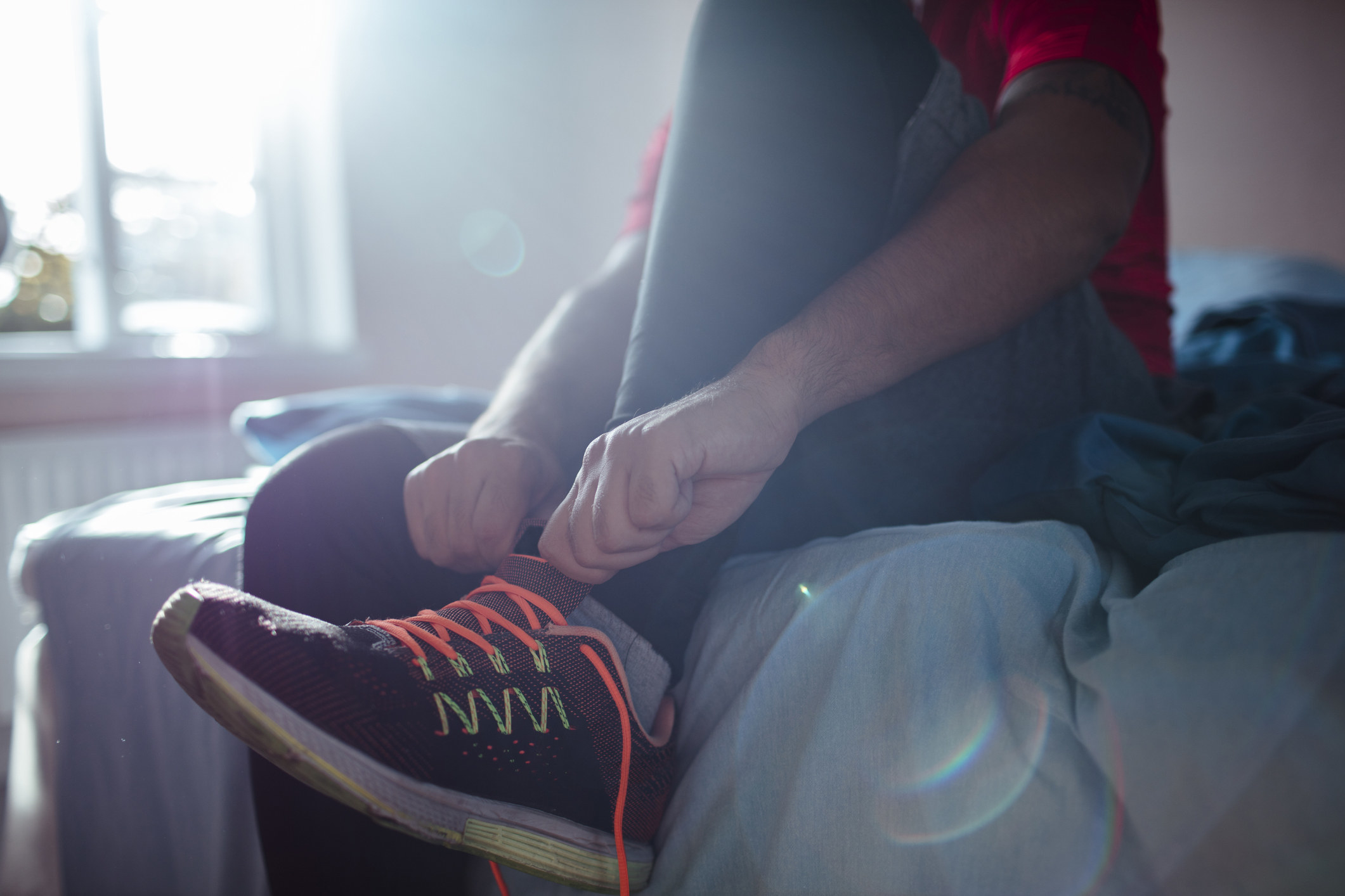 Someone sits on their bed and ties their sneakers, getting ready for a morning workout