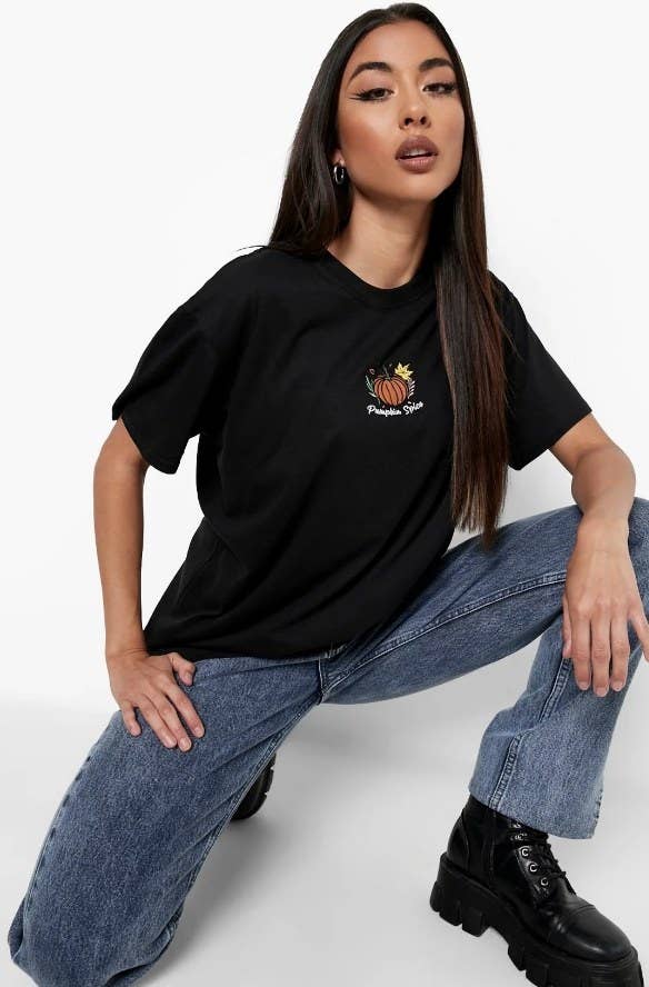 Model wearing black tee shirt with pumpkin embroidered decal in center