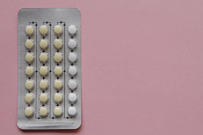 A stock image of a pack of birth control pills on a pink background