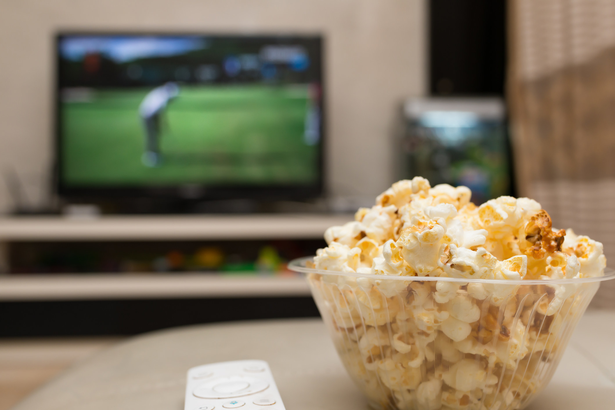 A bowl of popcorn and a TV remote with golf playing in the background