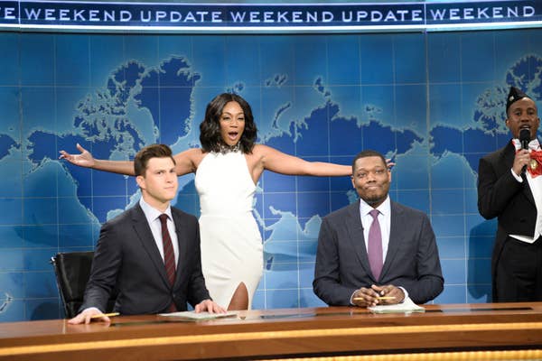 Tiffany Haddish crossing through the background of Weekend Update in a white gown