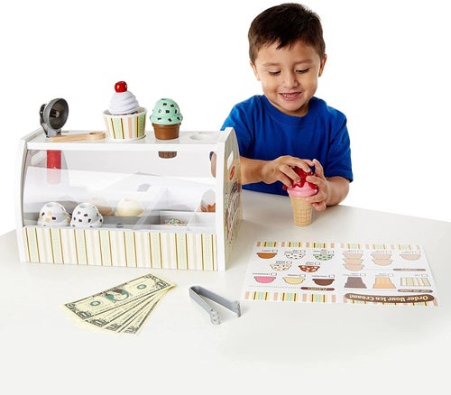 a child model adding a topping on an ice cream cone, while the stand, a menu and pretend money sits on the table
