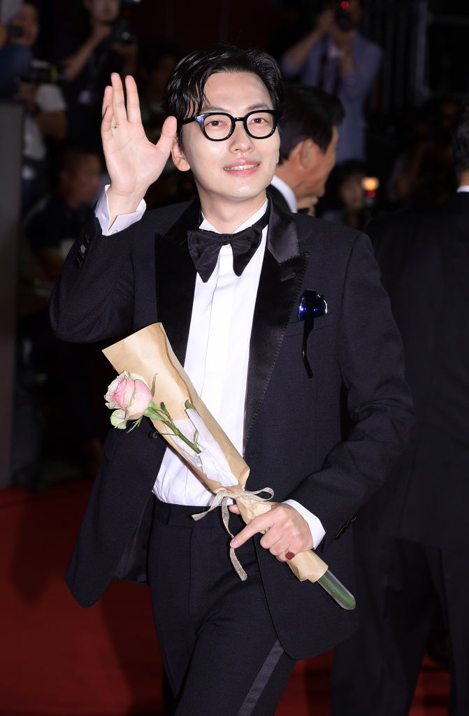 Dong-hwi Lee in a bow tie, waving and holding a flower on the red carpet