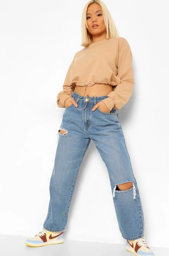 Model wearing baggy distressed boyfriend jeans with cropped tan shirt