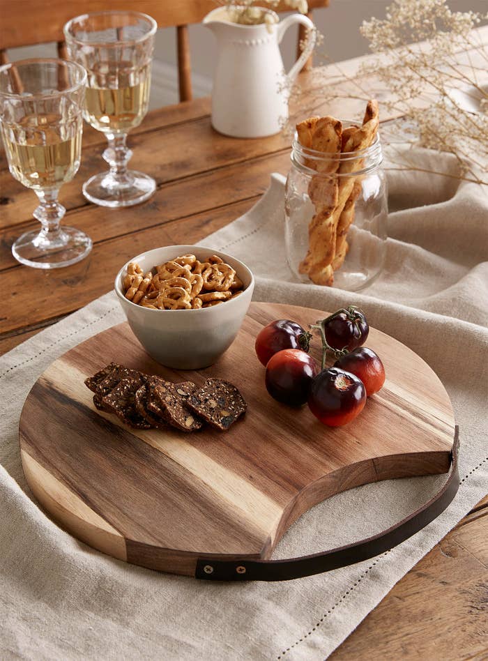 A round wooden tray with cheese, crackers, and fruit on it