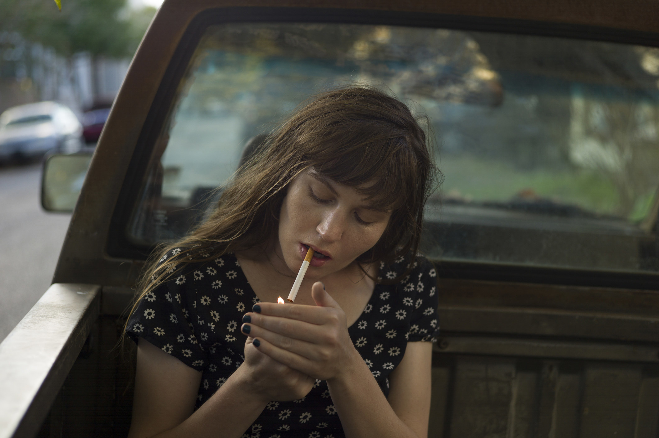 A woman lighting a cigarette in the back of a pickup truck