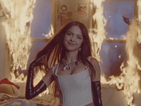 Olivia Rodrigo tossing her hair and smiling in a room that&#x27;s on fire