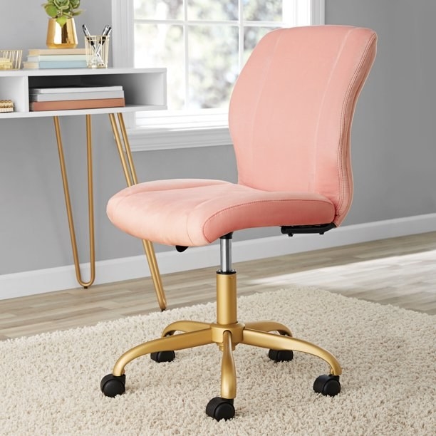 the pink velvet chair with gold legs on a carpet in front of a white desk with matching gold legs