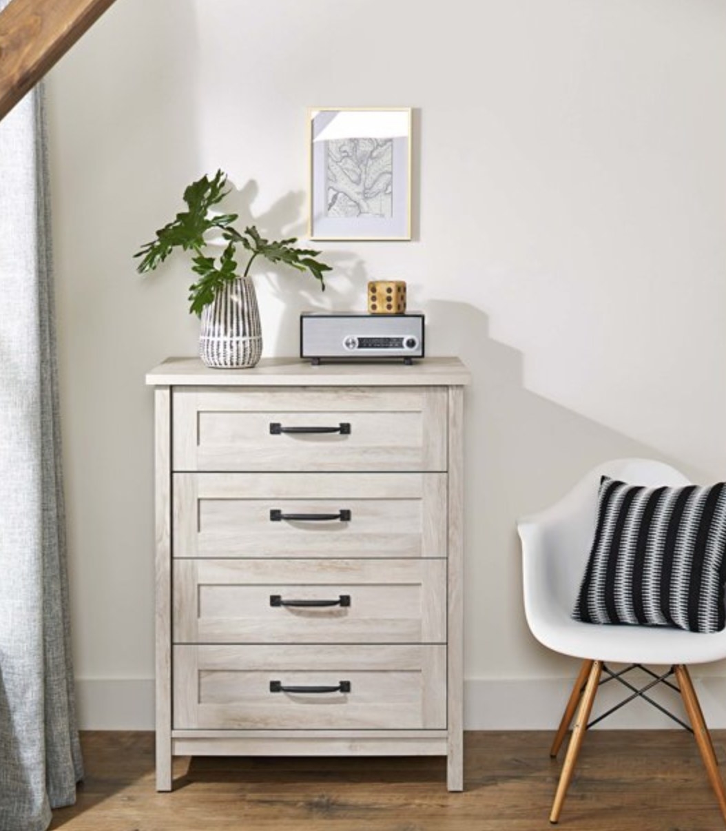 the four drawer chest with a plant and radio on top and a white chair next to it with a black and white pillow on top