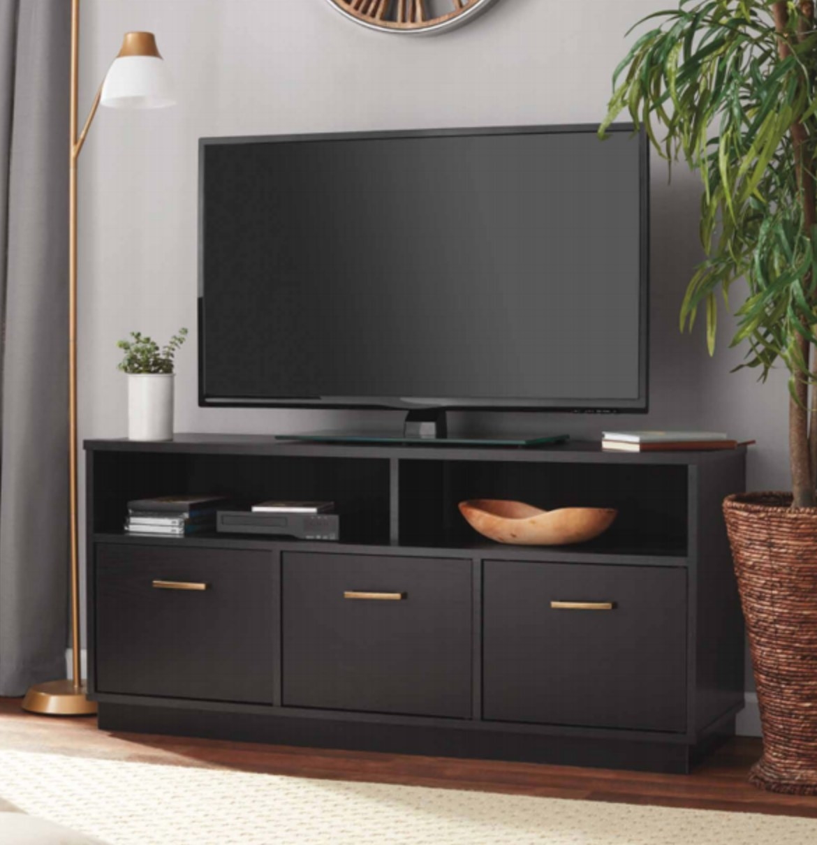 the black tv stand with three cubbies and two open shelves with a dvd player in the left shelf and a bowl in the right shelf