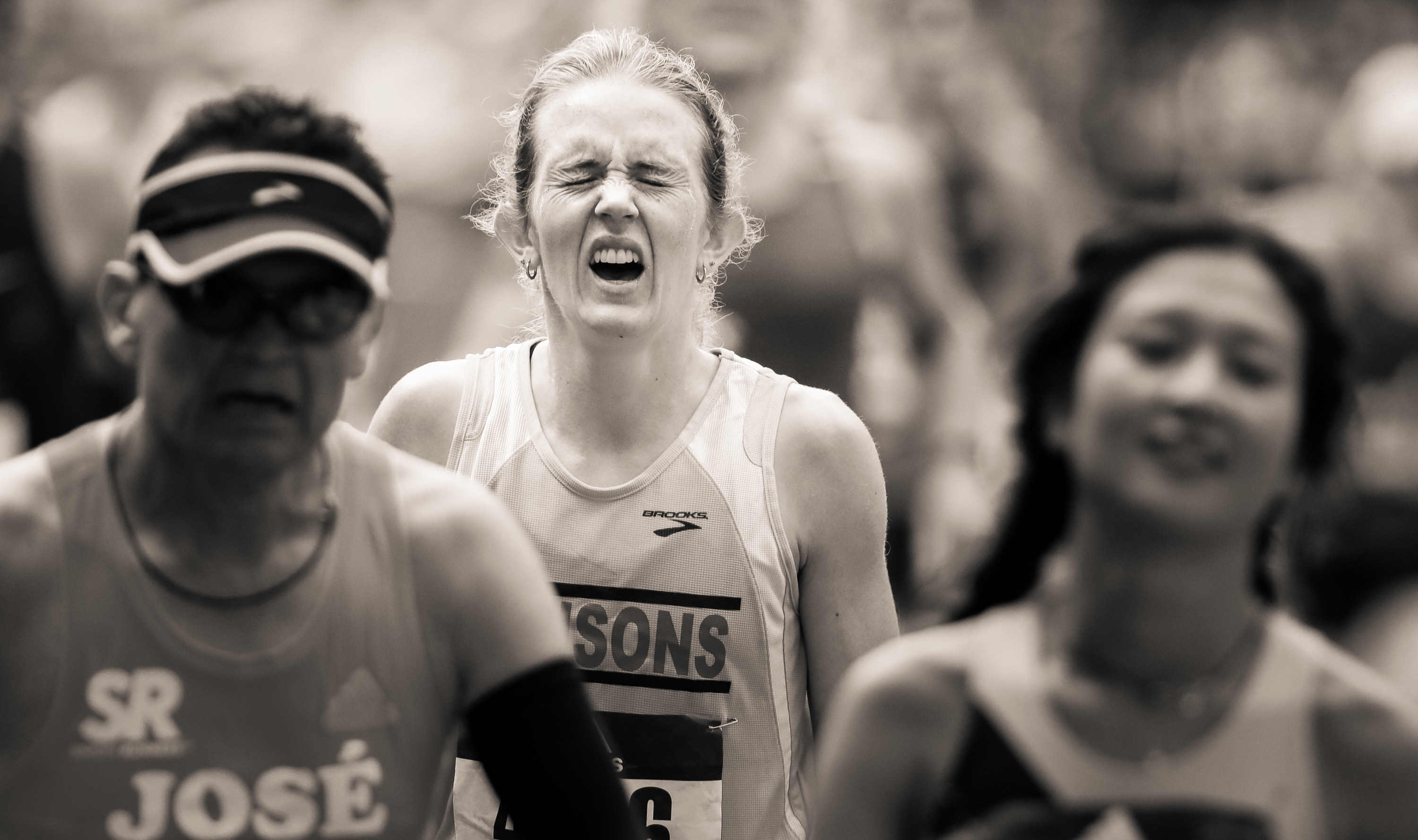 A woman grimaces through a crowd as she crosses the finish line