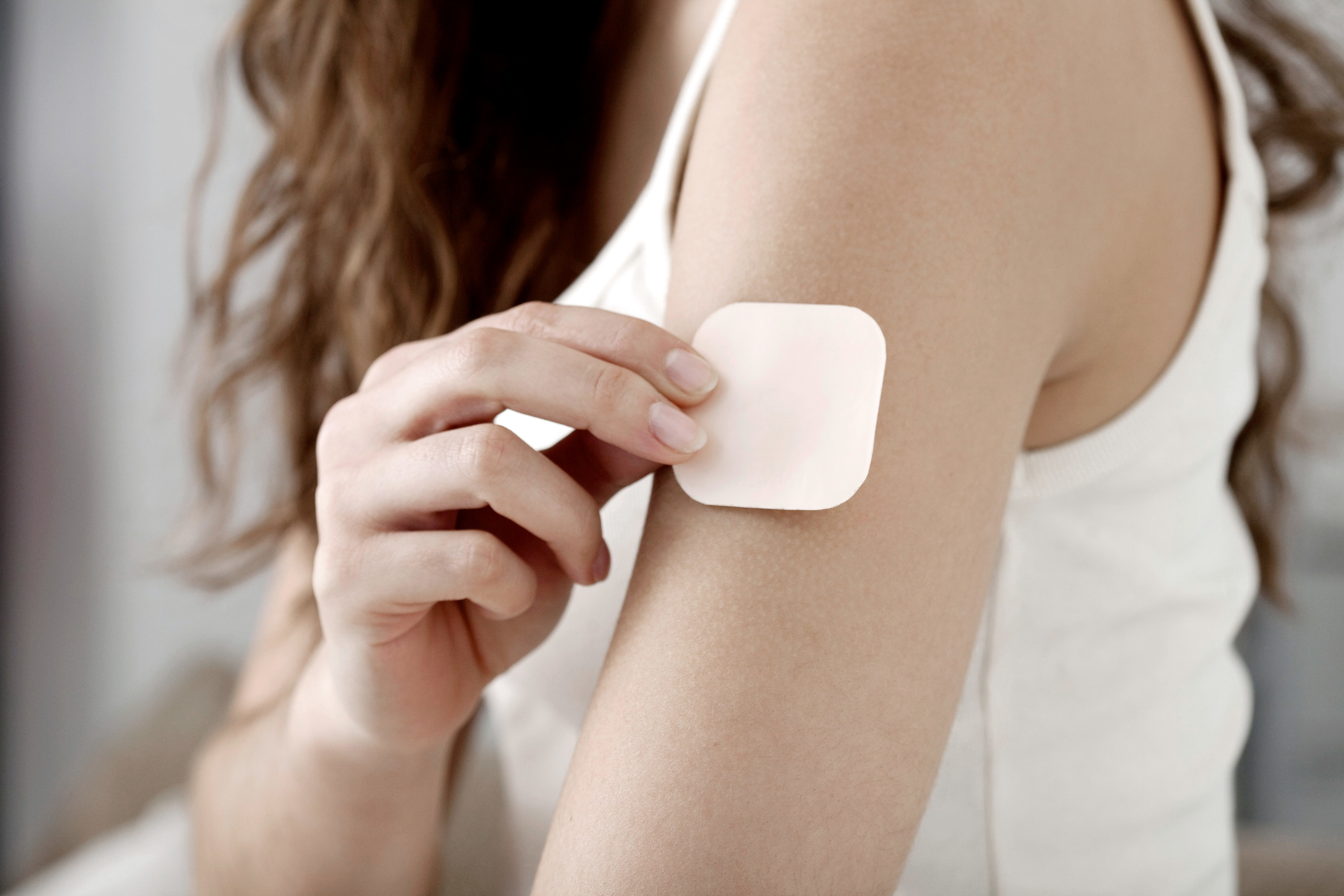 A stock image of a woman putting a birth control patch on her upper arm