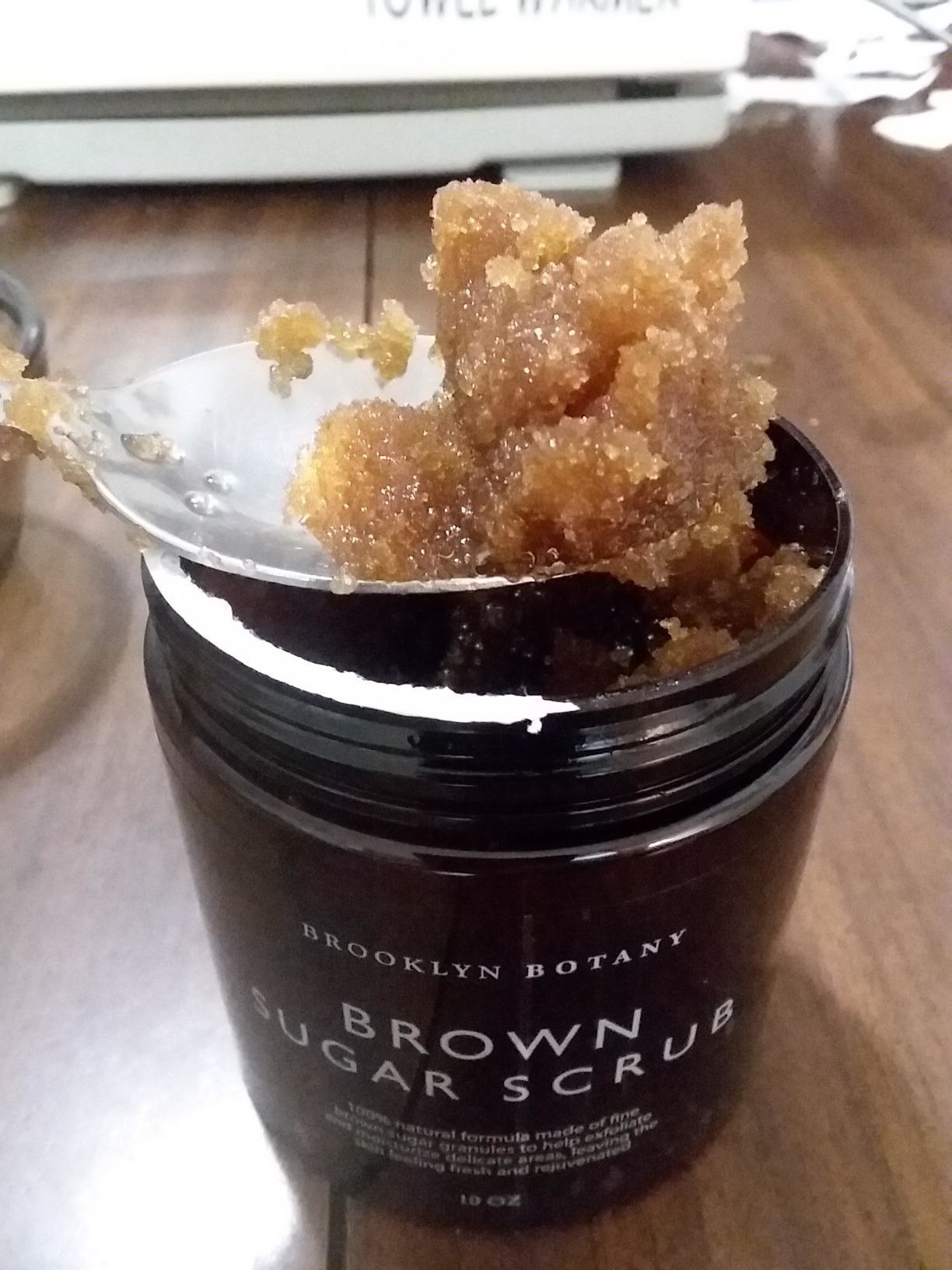 image of reviewer scooping brown sugar scrub out of jar with a spoon