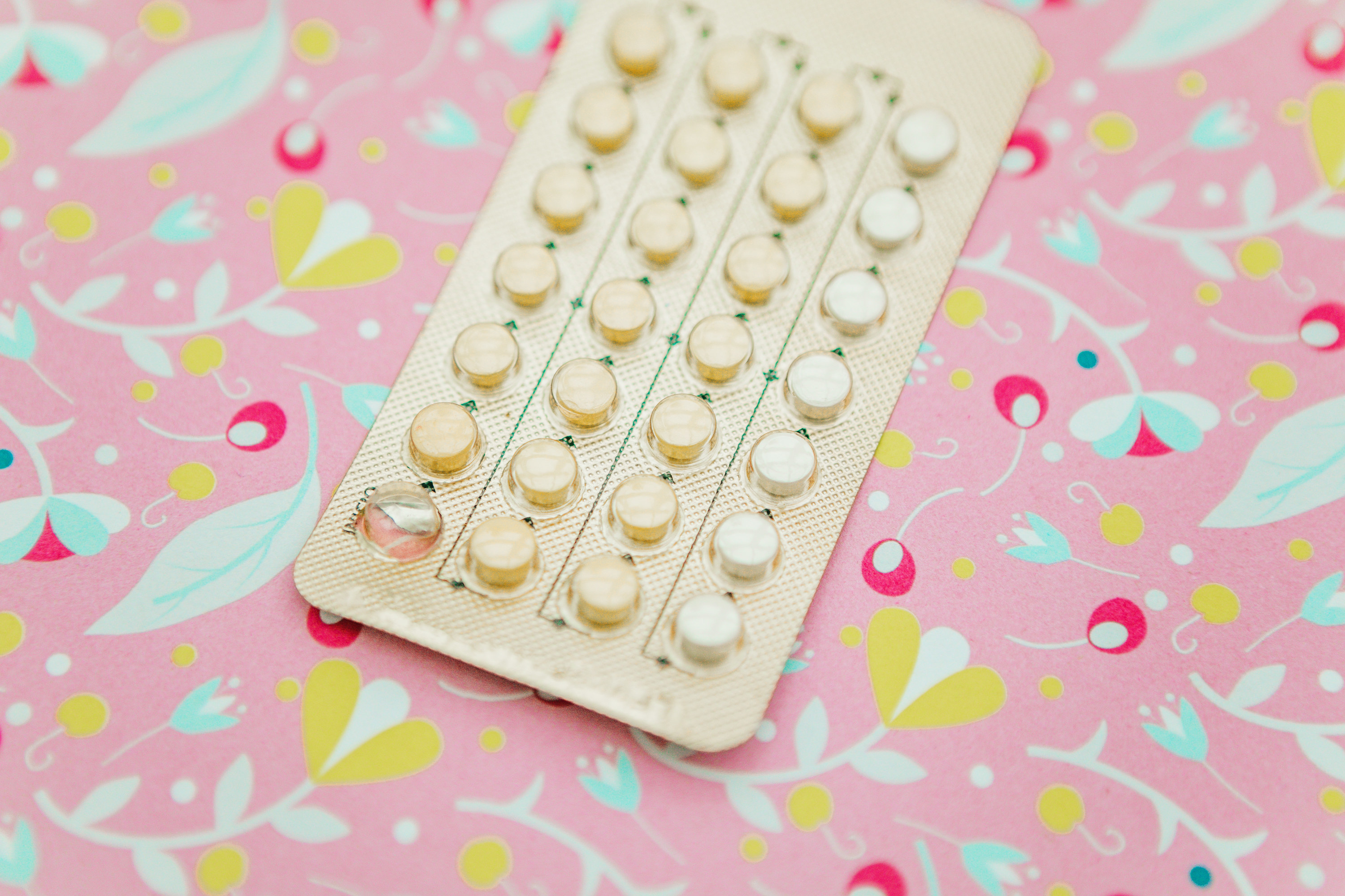 A stock image of a pack of birth control pills, on a colorful pink flowery background