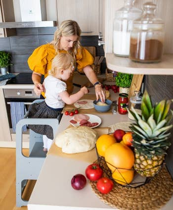 Parent and child cooking at the kitchen counter with the child standing on a gray step stool with safety bars installed around the edges