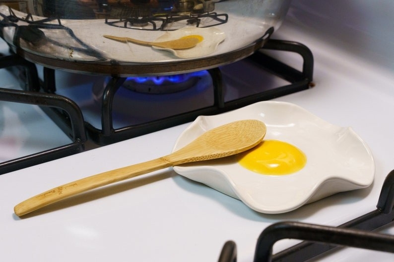 egg-shaped spoon rest with wooden spoon on top next to silver pan