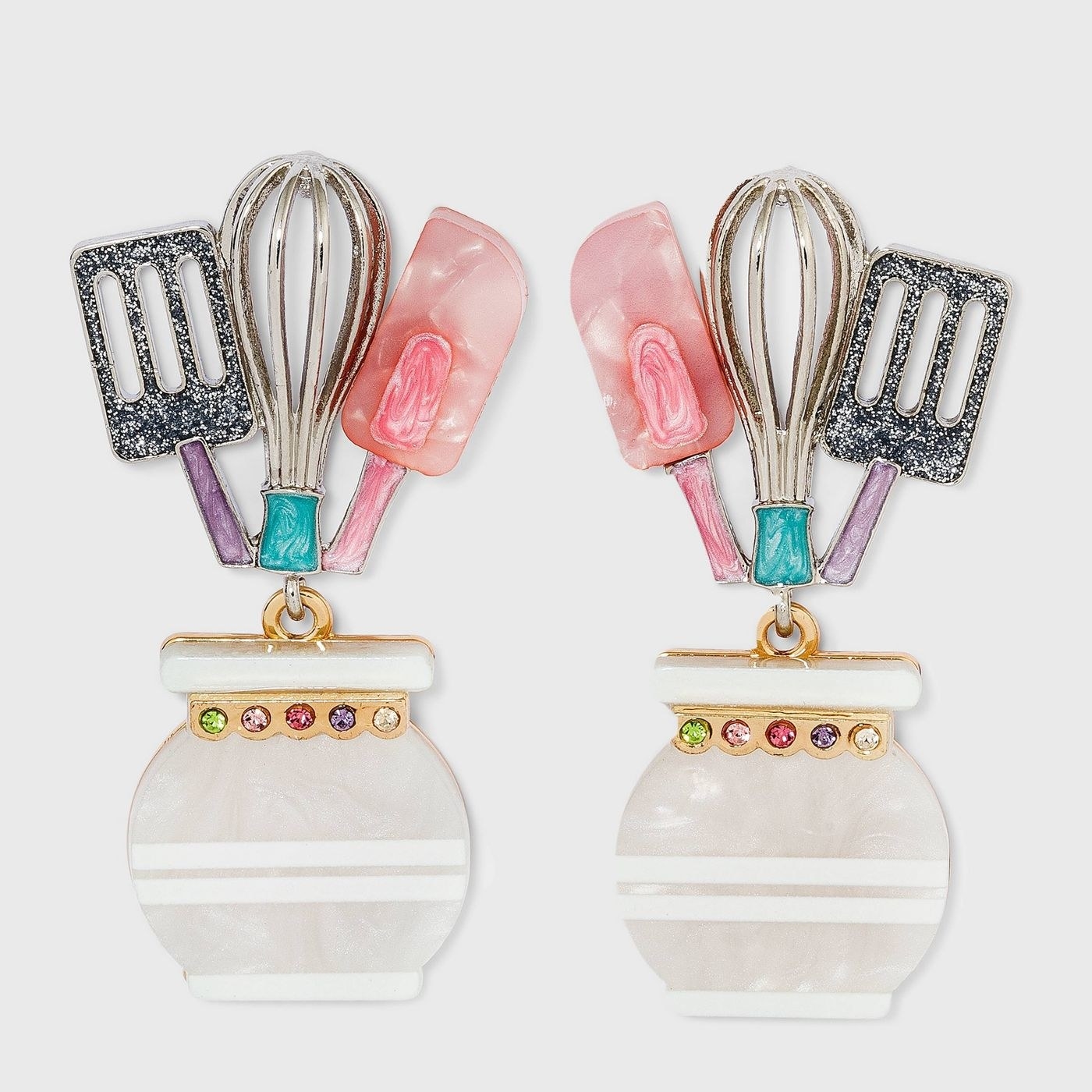 white, pink, purple, silver, and teal drop earrings shaped like spatulas and a whisk in a utensil holder