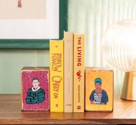 block-shaped bookends with designs of feminist icons holding up stack of books