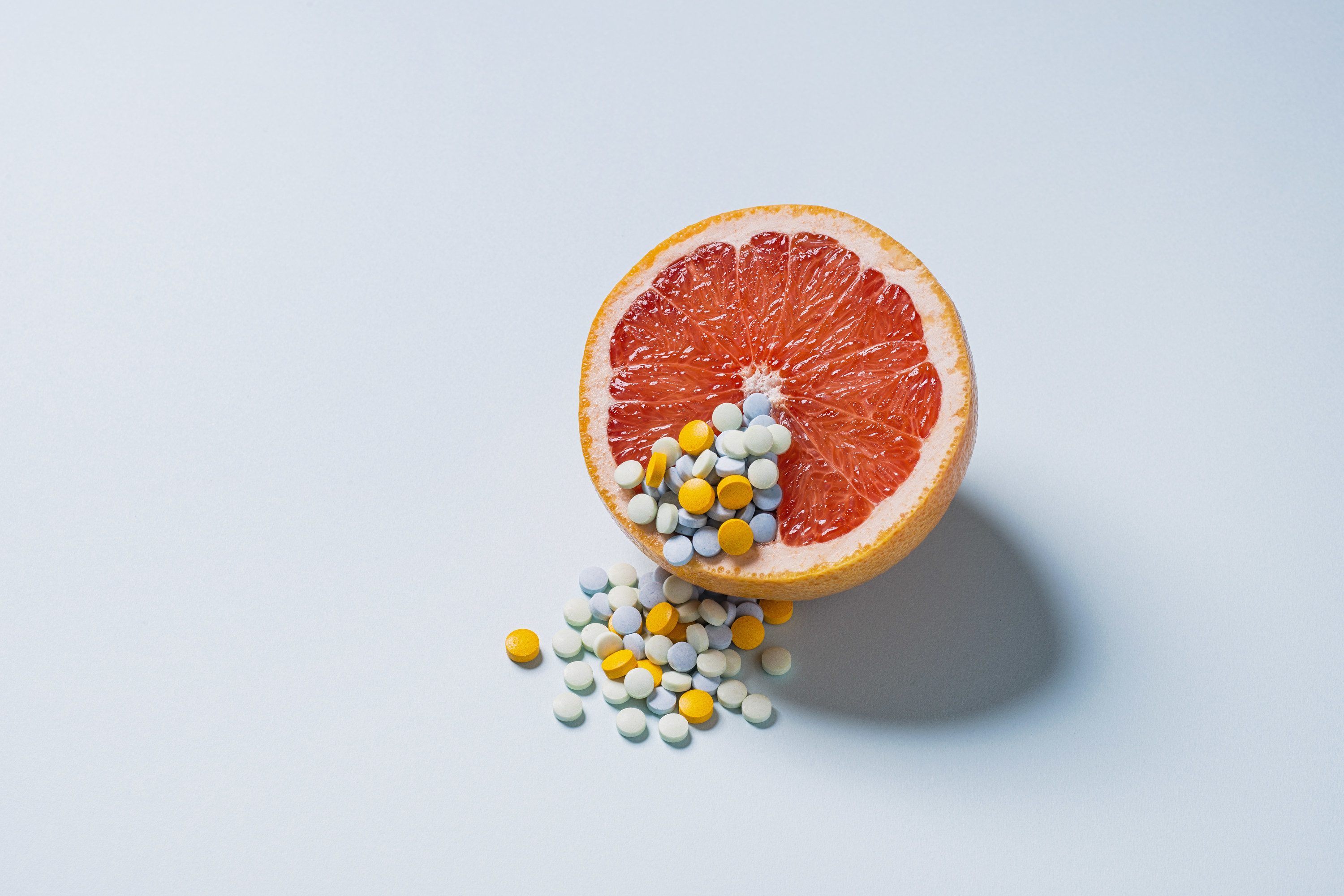 A stock image of a grapefruit with pills surrounding it
