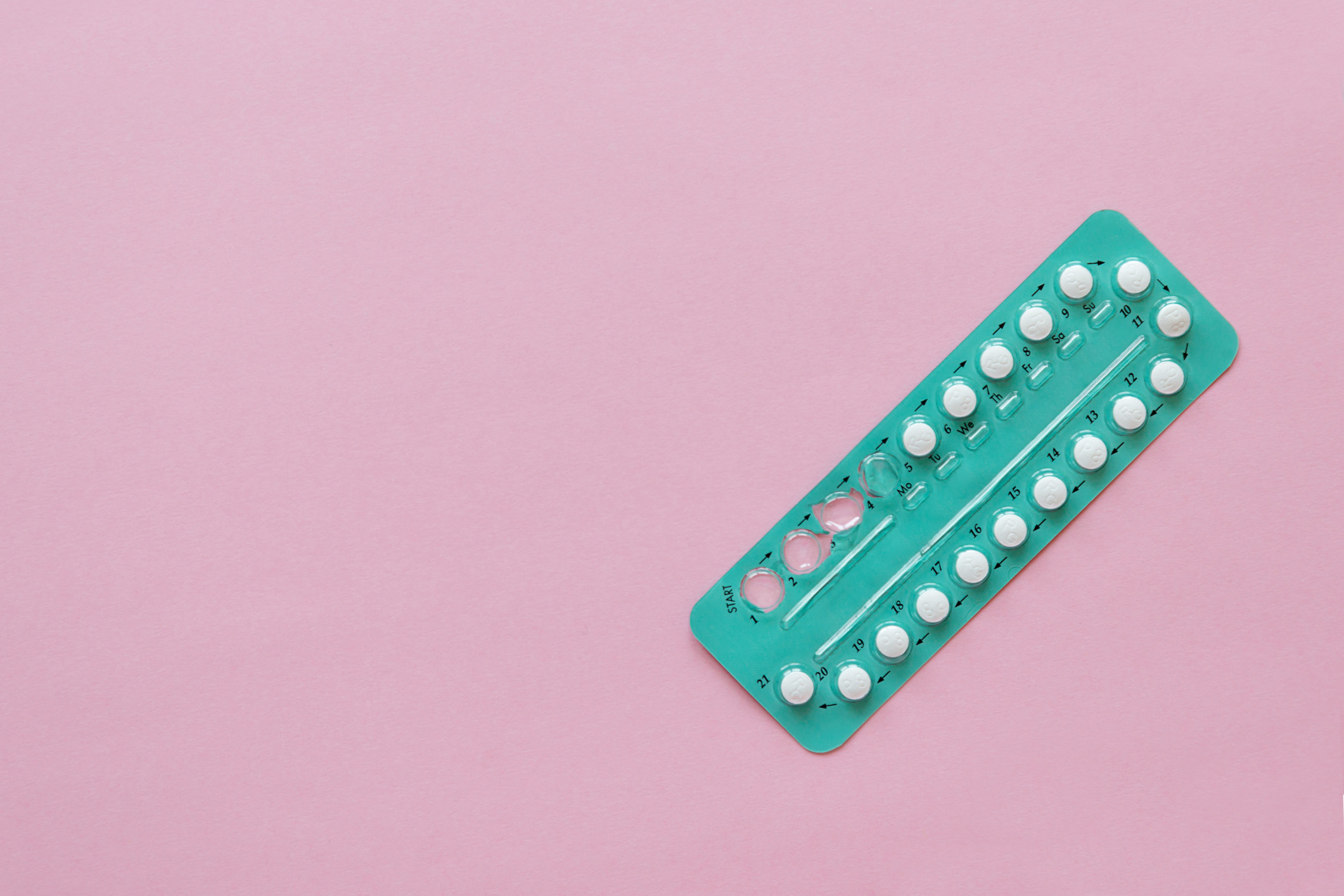 Stock image of birth control oral contraceptives in a green pack on a pink background