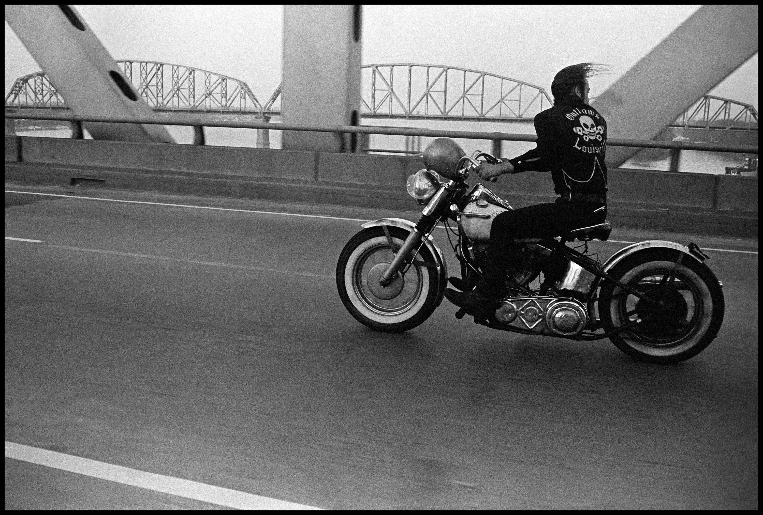 A man rides a motorcycle over a bridge